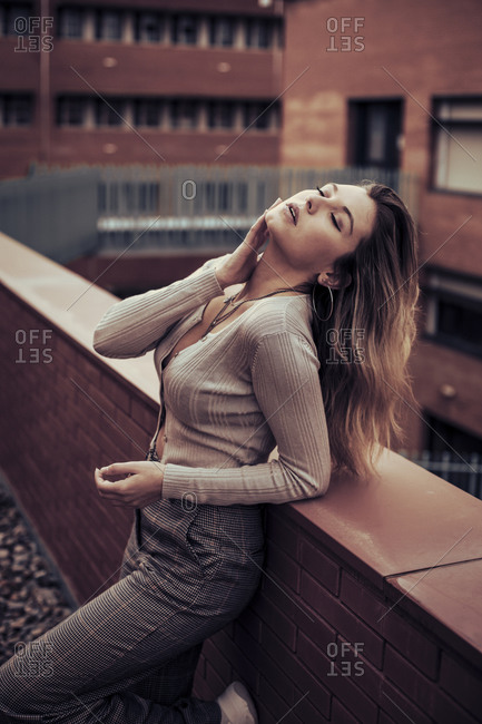 Blonde woman posing seductively and touching her face on a red brick wall