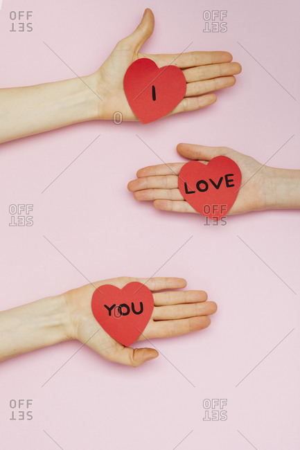 Three hands holding Valentine hearts that read 