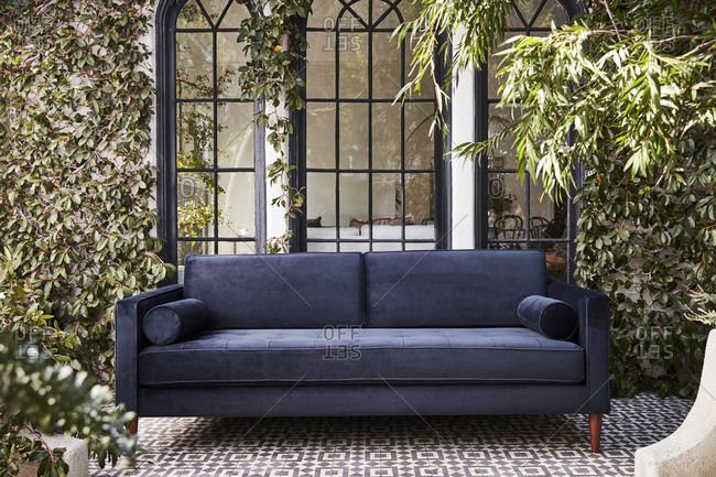 Blue velvet sofa on tile patio in front of large windows