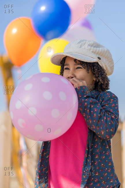 African-American girl with curly hair blowing up a pink balloon