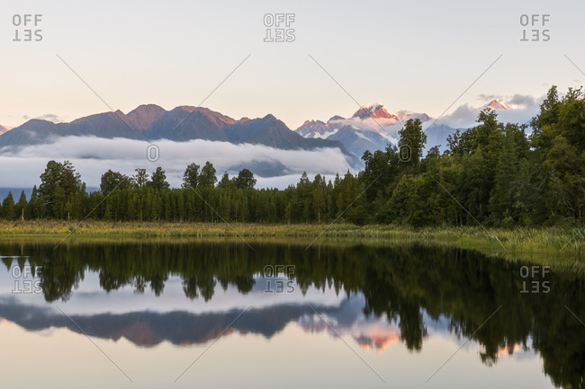 New Zealand- Westland District- Fox Glacier- Lake Matheson reflecting surrounding forest and distant mountain range