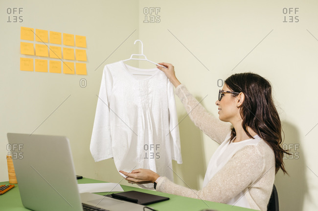 Young woman sitting at desk in office examining garment