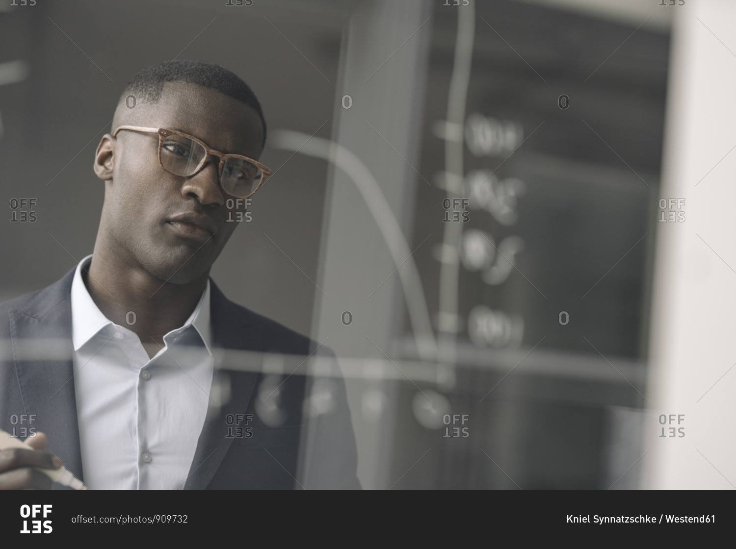 Portrait of young businessman looking at diagram on glass pane in office