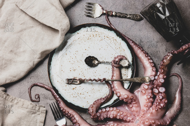 octopus holds forks and knife with tentacles on a table