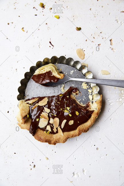 Half eaten chocolate ganache tart with a spoonful on a white background,