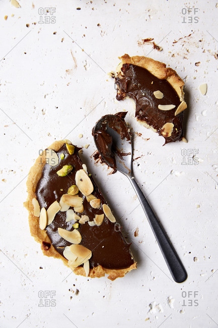 Half eaten decadent chocolate ganache tart with a spoonful on a white background,