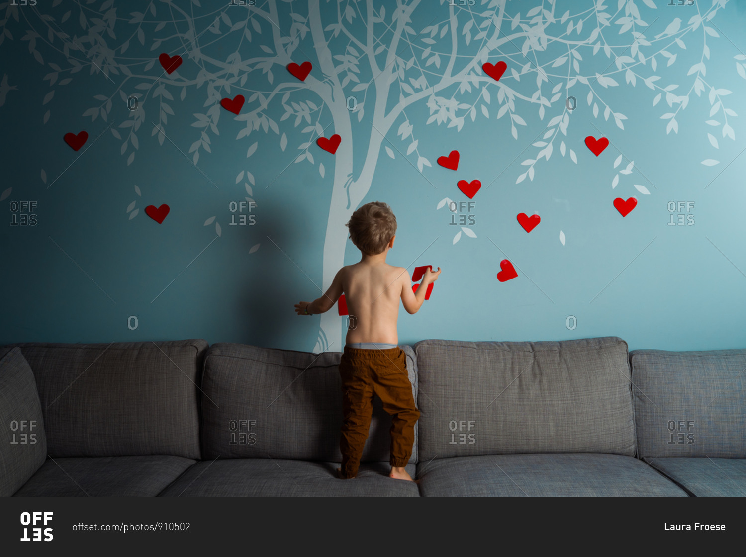 Toddler decorating a wall decal of a tree with red hearts for valentines day