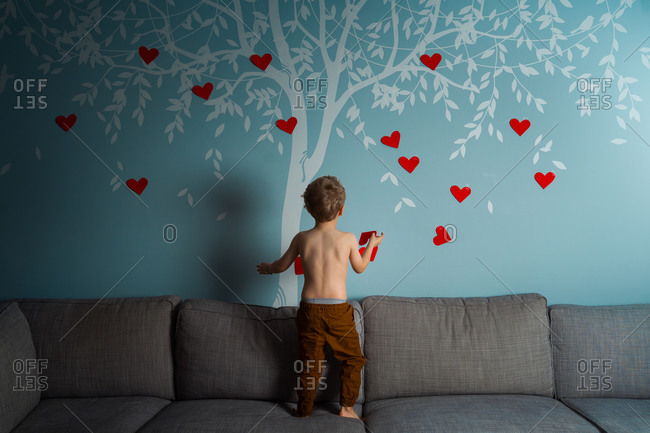 Toddler decorating a wall decal of a tree with red hearts for valentines day