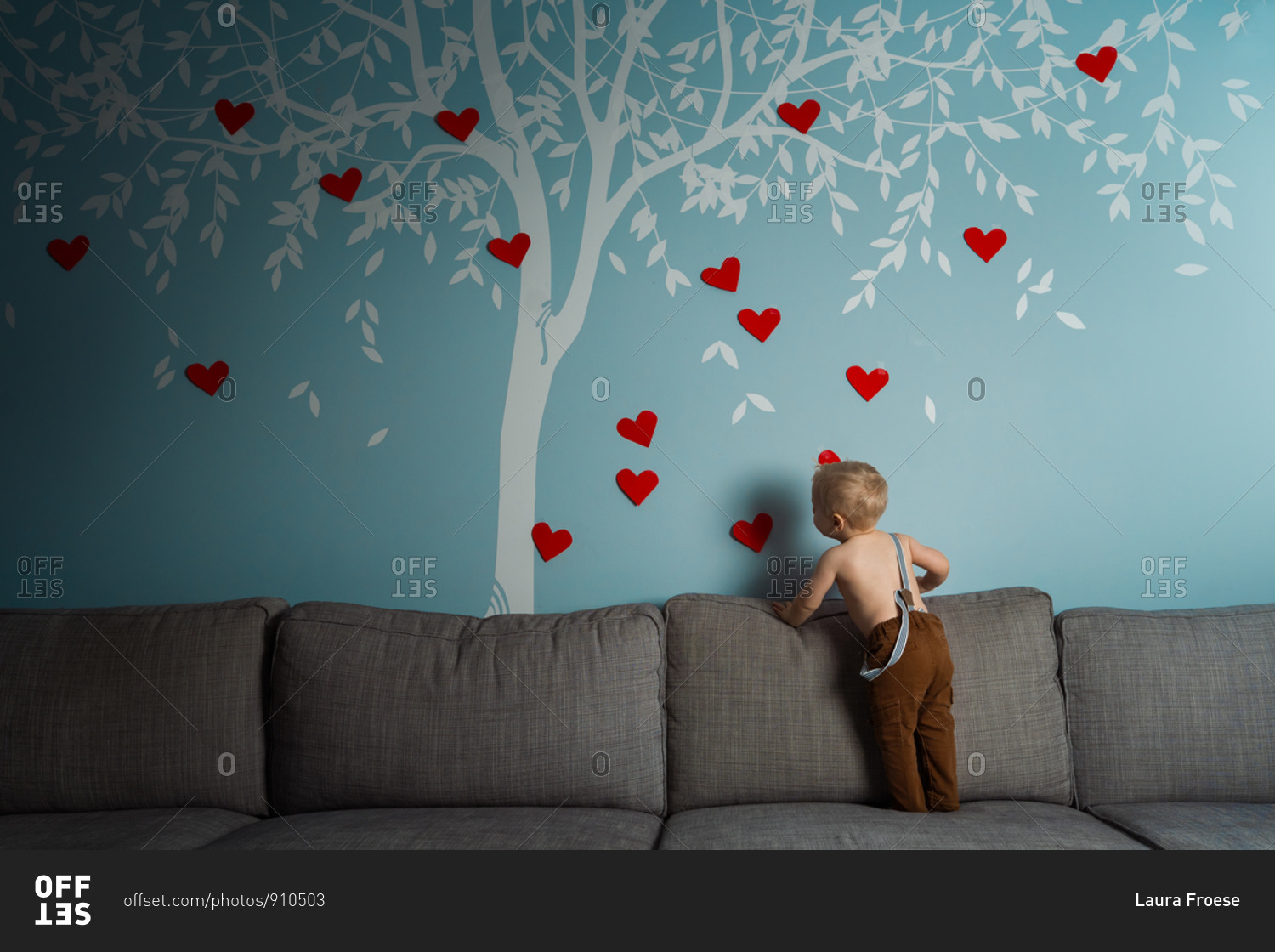 Cute toddler decorating a wall decal of a tree with red hearts for valentines day