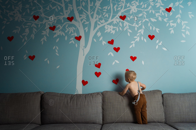 Cute toddler decorating a wall decal of a tree with red hearts for valentines day