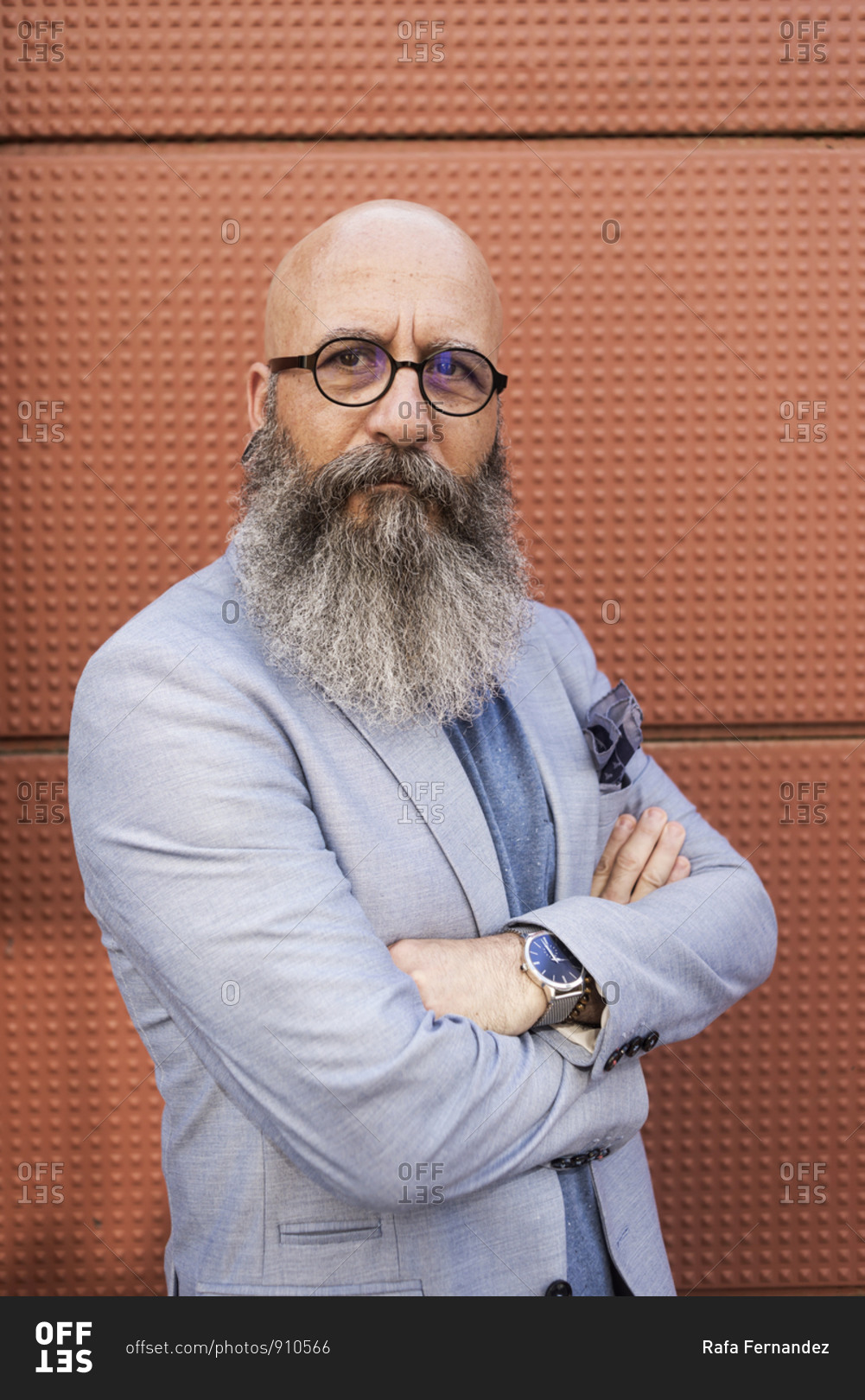 Portrait of a hipster bearded mature man wearing blue jacket and eyeglasses arms crossed outdoors