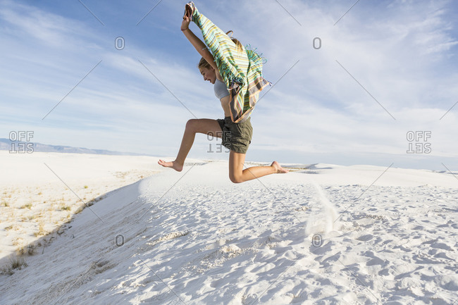 A teenage girl leaping in the air, in a wide open space, sand dunes.
