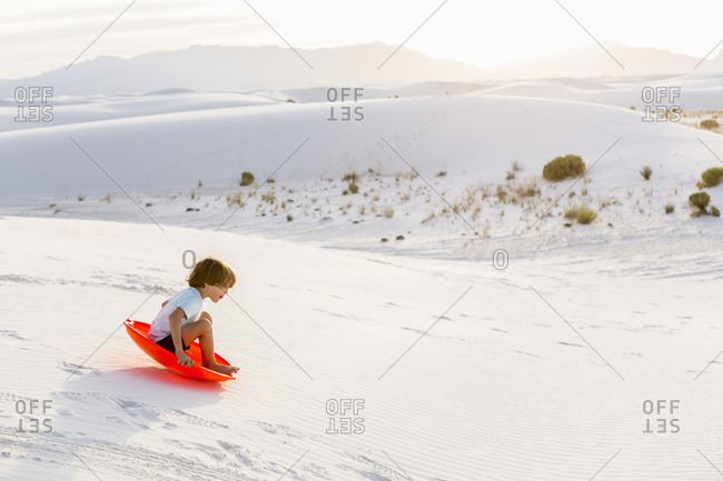A young boy sledding down white sand dunes