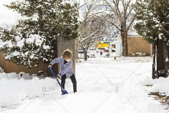 A young boy shoveling snow in driveway