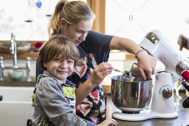 A teenage girl and her 6 year old brother in a kitchen, using a mixing bowl