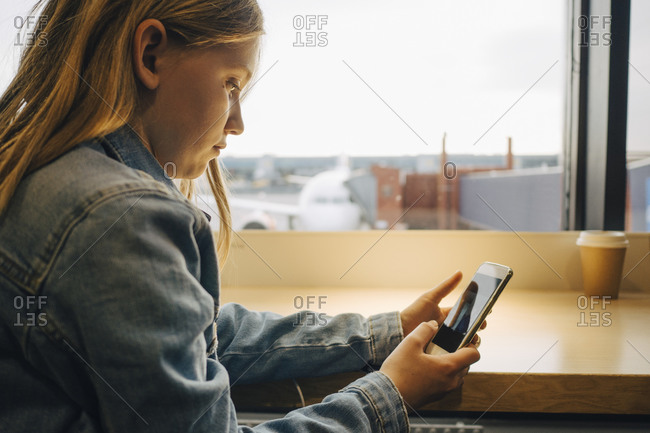 Side view of girl using mobile phone while sitting at airport