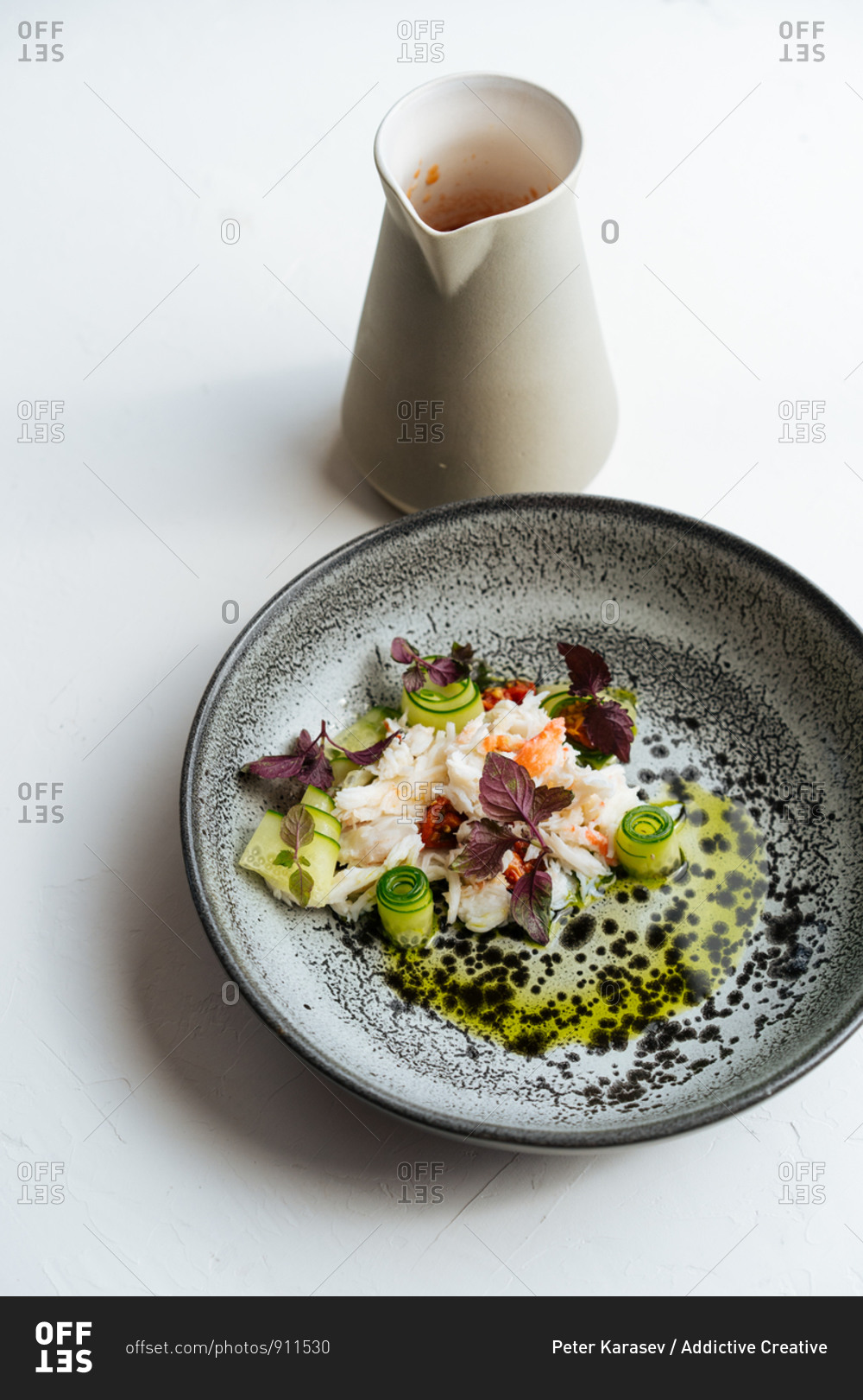Top view of crab core with cucumbers and basil placed on plate near jug with tomato sauce on white background