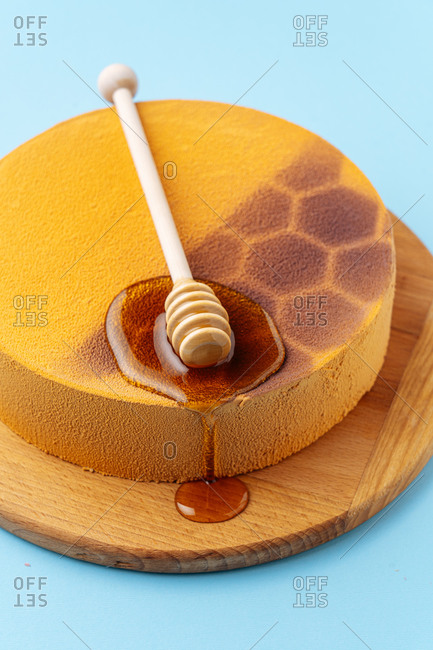From above delicious honeycomb cake decorated with spoon and fresh liquid honey on blue background
