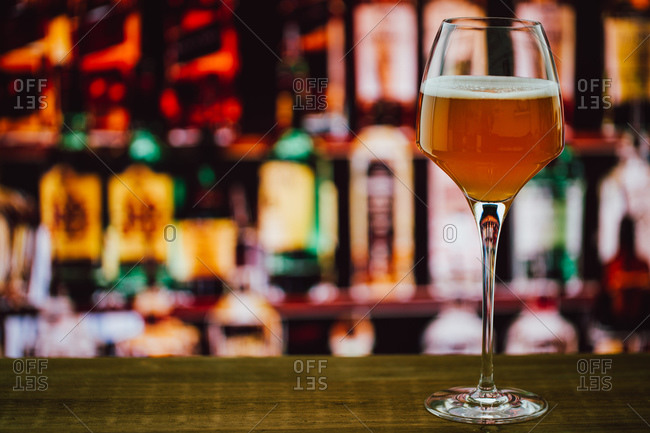 Beer in wineglass with foam in glass on wooden counter in bar on blur  background stock photo - OFFSET