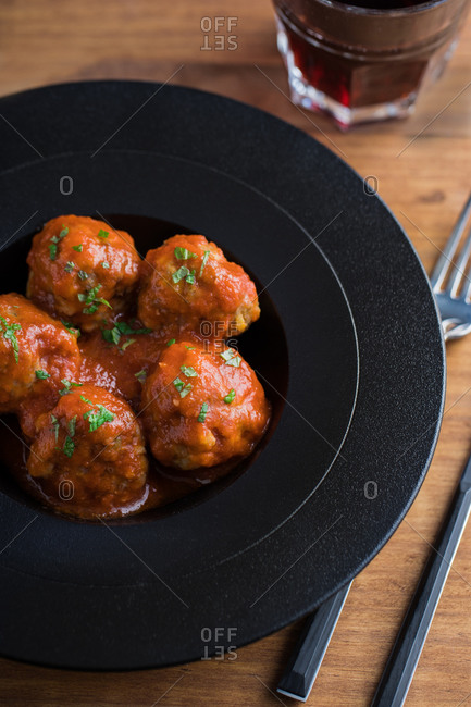 From above tasty cooked meatballs with tomato sauce serving with bread on black plate with cutlery and beverage on table
