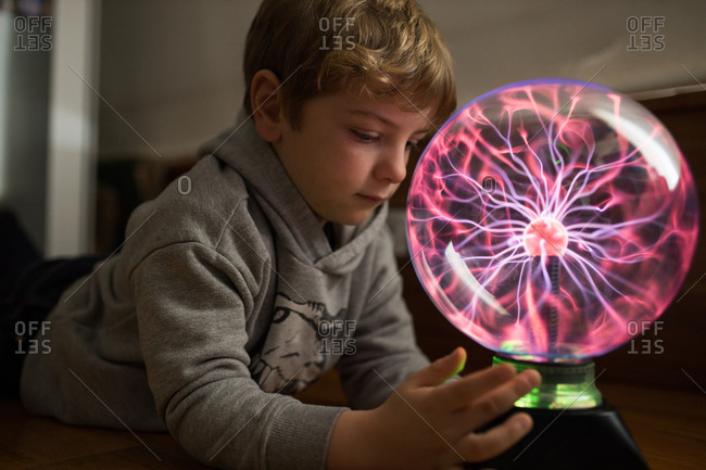 Side view of pensive child concentrating on looking at round lamp with pink neon streams at table