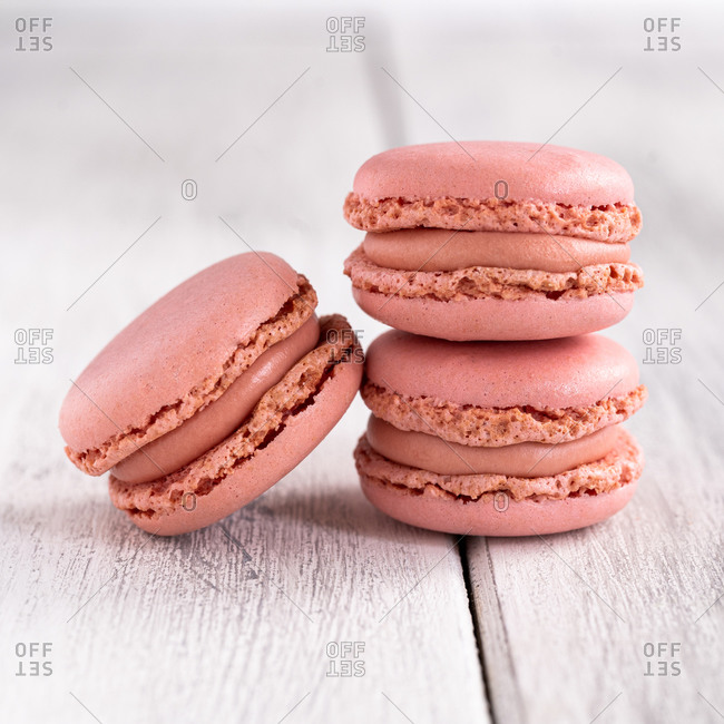 Pink tasty macaroons stacked in pile against wooden white surface