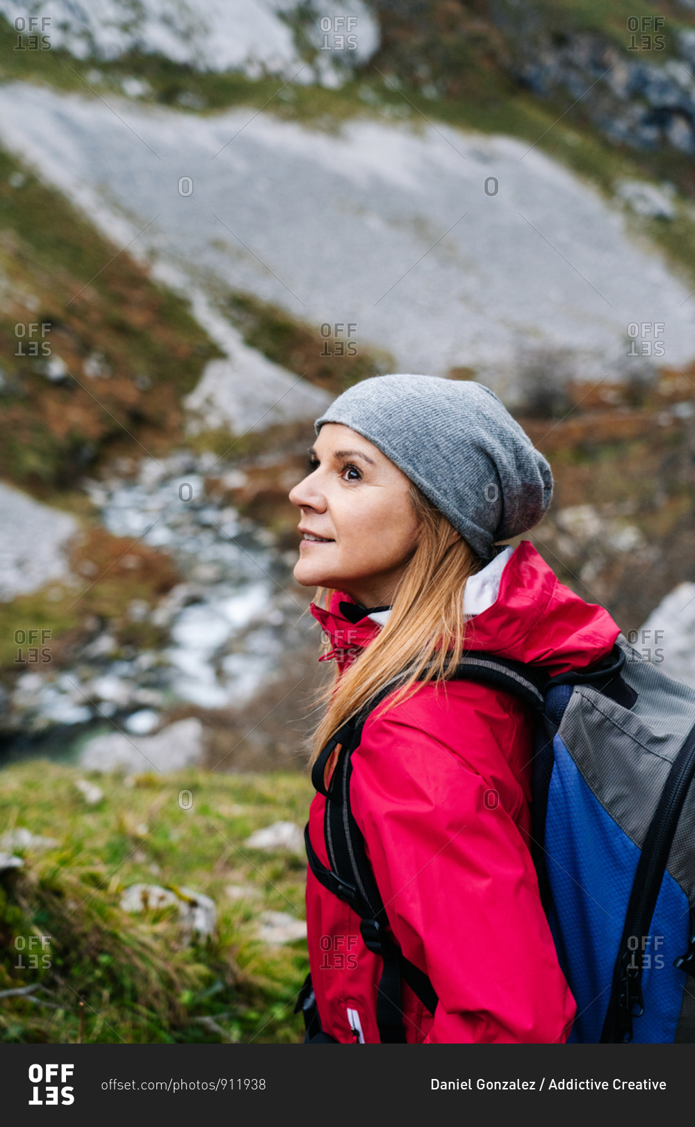 Side view of active woman hiker in red jacket with heavy backpack looking away while walking in mountain in peaks of Europe, Asturias, Spain