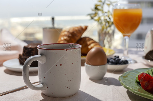 Homemade full brunch breakfast in sunlight with cooked eggs, blueberries, sponge cake, croissants, toast, tea, coffee and orange juice