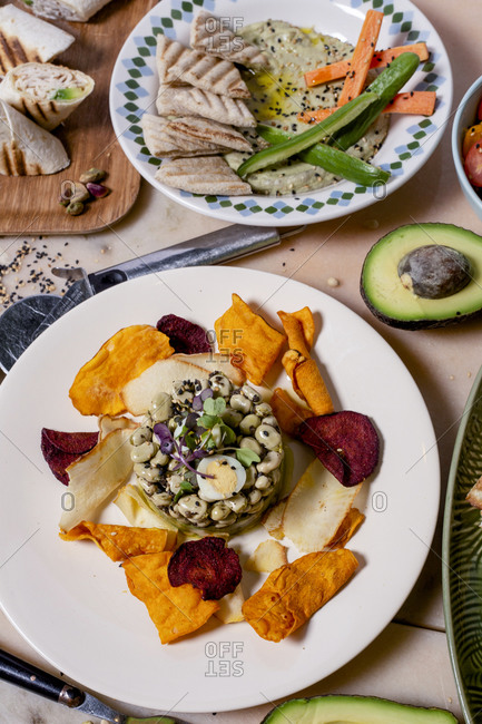 From above of dish of bean with petals on plate near fork with knife and pizza on table