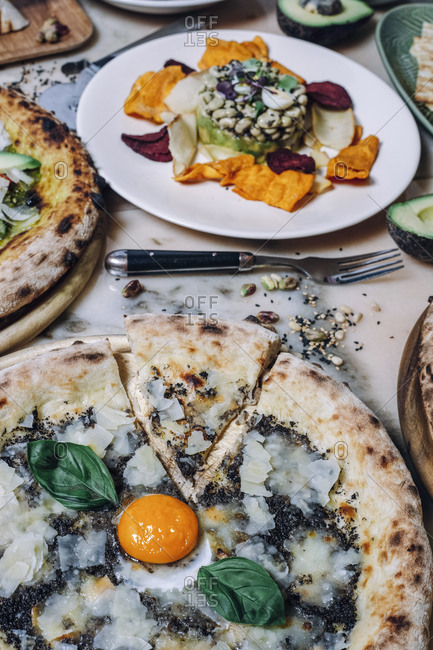 From above of dish of bean with petals on plate near fork with knife and pizza on table
