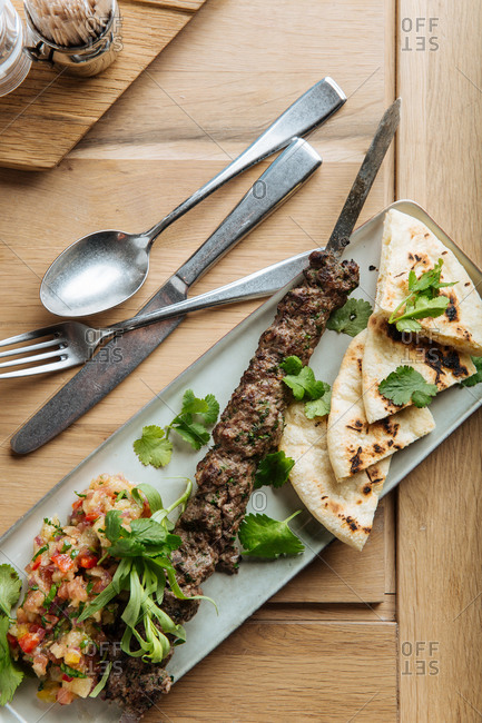 Top view of kebab and flatbread served with fresh herbs on wooden table in restaurant