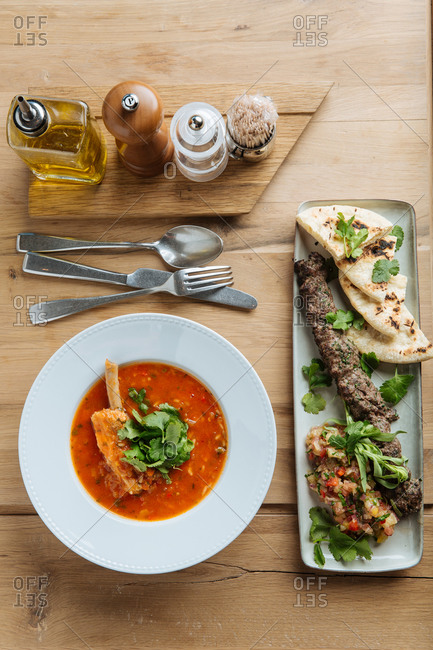 Top view of red soup with meat and fresh herbs on wooden table with kebab and flat bread in restaurant