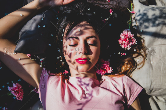 Brunettete girl slipping in a bed with flower petals, shadows on a face. Above view