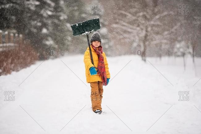 Boy with a shovel standing in the snow on a long snow covered driveway, Wisconsin, USA