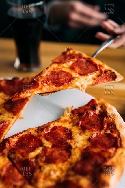 Human hand serving a slice of pepperoni pizza
