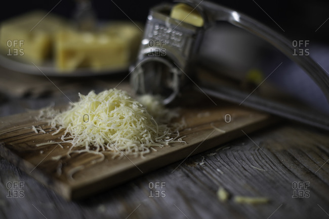 Parmesan Cheese and Grater Above. an above view of a block wedge of  parmesan cheese with shredded pieces all around and a metal cheese grater  on a cutting board Stock Photo