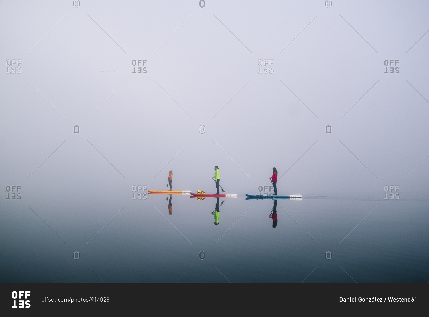 Three people stand up paddle surfing on a lake in the fog