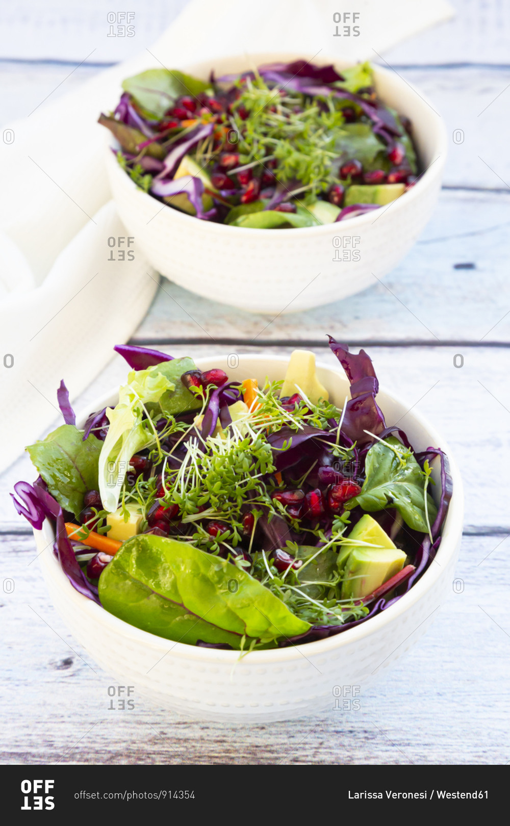 Two bowls of salad with red cabbage- carrots- lettuce leaves- avocado- pomegranate seeds and cress