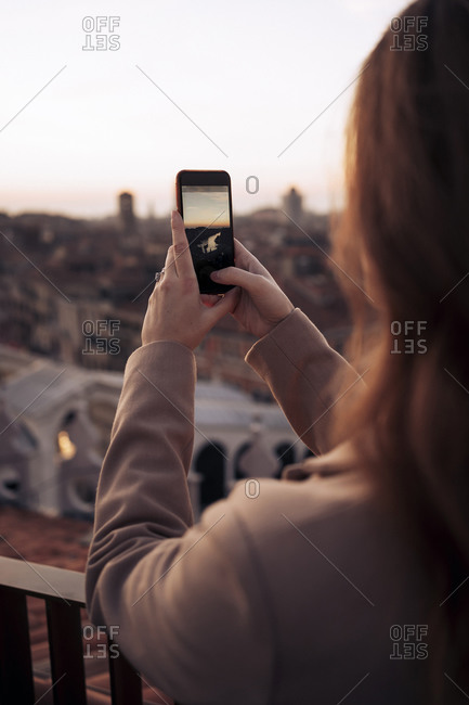 Young woman taking cell phone picture on a balcony above the city of Venice- Italy