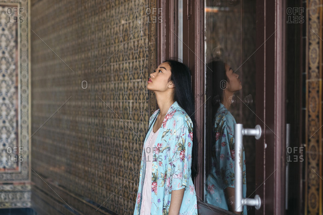 Portrait of beautiful young woman wearing a kimono leaning against a door with reflection