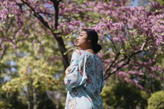 Beautiful young woman with blooming cherry tree in a public garden in spring