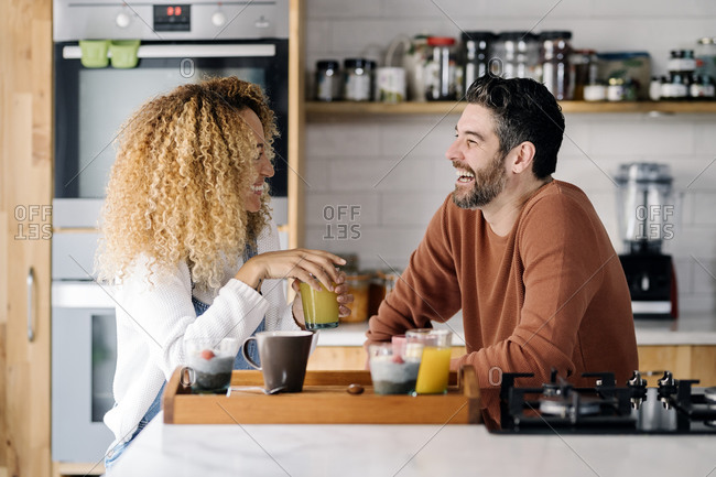 Stock photo of a middle aged woman and man having breakfast in a kitchen and laughing together. They are relaxed.