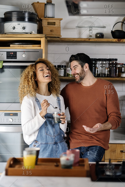 Stock photo of an unrecognizable middle aged woman and man standing in a kitchen and laughing. They are having a conversation.