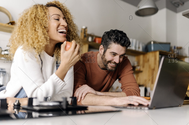 Stock photo of a middle aged woman and man standing in a kitchen and looking at a laptop. They are smiling.