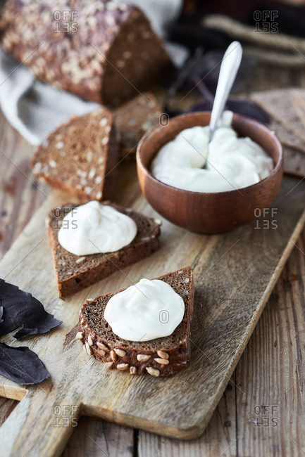 Sour cream on black bread with sunflower seeds on a wooden board