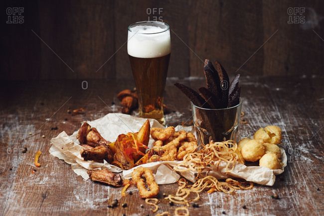 Glass of beer with chicken wings, french fries, squid rings, cheese balls, onion rings, and crackers