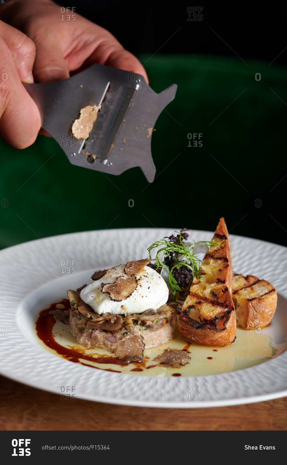 Hands shaving truffle over a dish of poached egg and mushrooms with