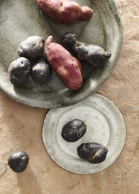 Sweet potatoes and black potatoes on grey stone platters