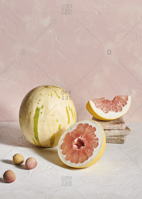A pomelo fruit, lychees and an unusual speckled melon on textured plaster surfaces