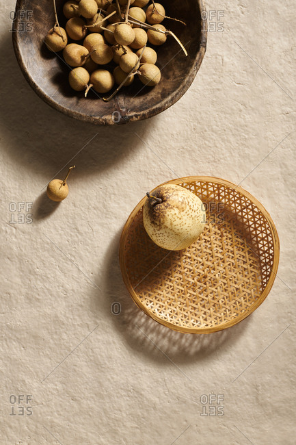 A wooden bowl of longan fruit and an Asian pear in a woven bamboo basket